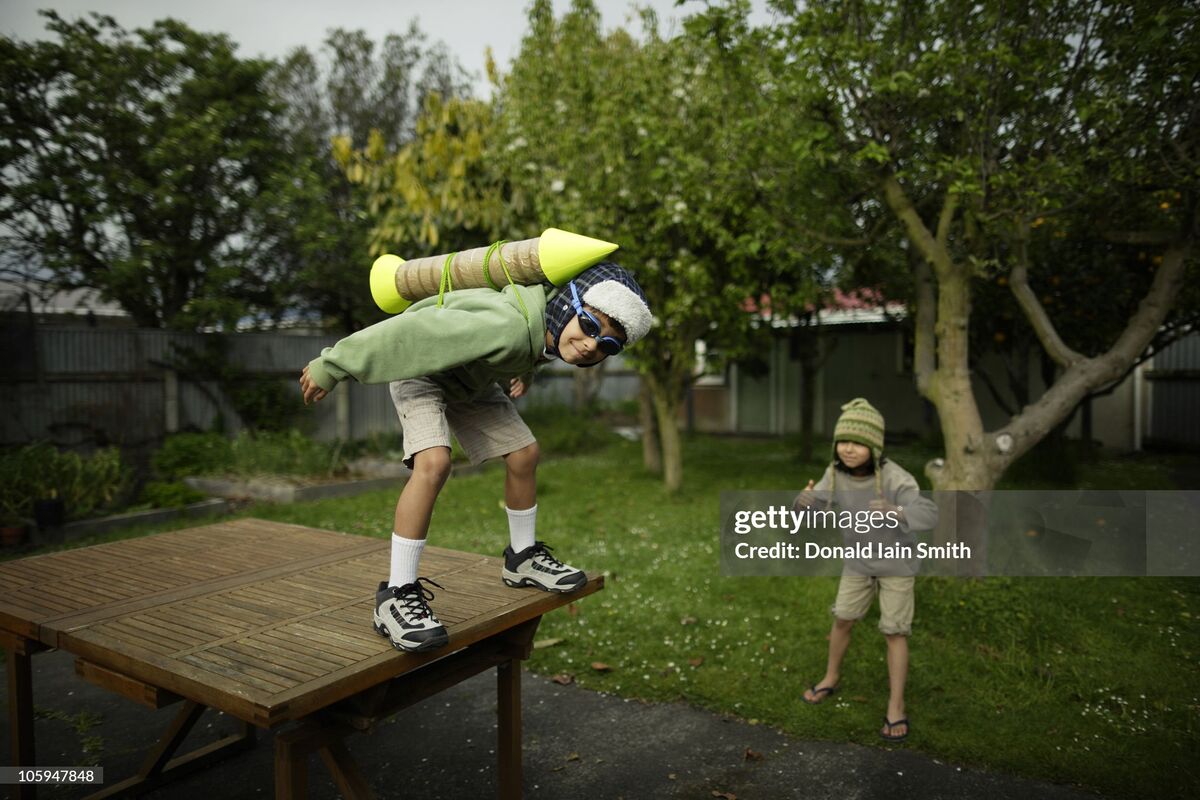 Josh in swim goggles and a homemade cardboard rocket pack, crouched on a garden table ready to jump